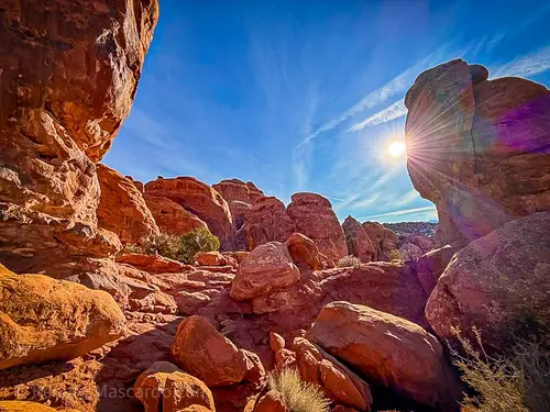 Sunlight streaming through rock formations in Arches National Park, highlighting red sandstone against a clear blue sky.